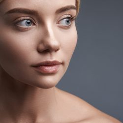Peaceful young beautiful woman thoughtfully looking into the distance while having laconic make up and standing against the grey background